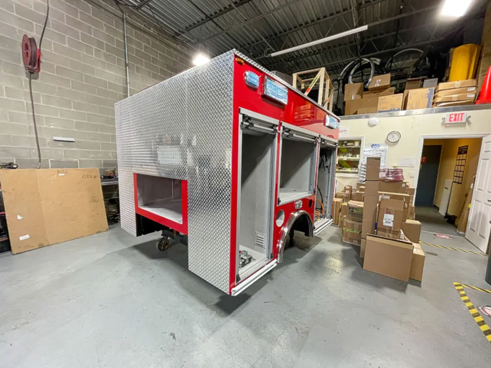 Exterior view of small fire truck showing cab, body compartments, and wheel/tire area.